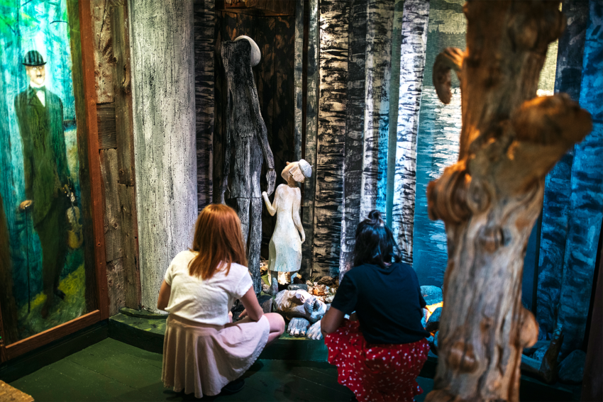 Two girls are visiting the museum about the storytelling network in Kronoberg and are in a room that is set up as a forest.